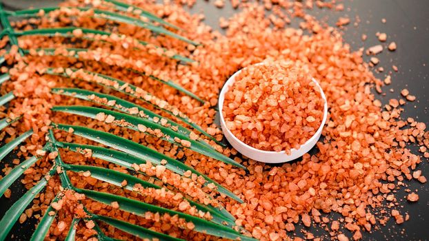Orange sea salt on a black background. Tropical palm leaves on background. Beauty concept. Spa background with a space for a text