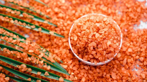 Orange sea salt on a white background. Tropical palm leaves on background. Beauty concept. Spa background with a space for a text