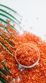Orange sea salt on a white background. Tropical palm leaves on background. Beauty concept. Spa background with a space for a text