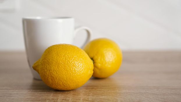 Two lemons on the kitchen table near a white mug of tea. Morning concept