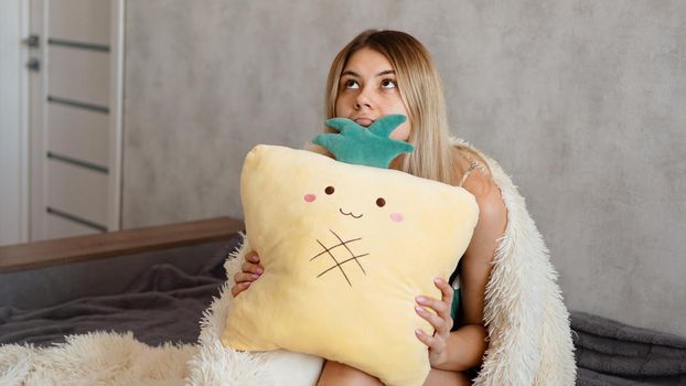 Young woman sitting on sofa and thinking. Beautiful girl holding cushion and looking serious or sad