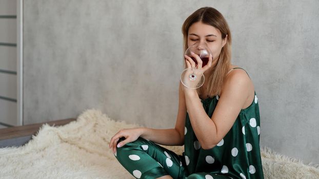 Girl in green pajamas in bed with a glass of red wine. Morning wine in bed