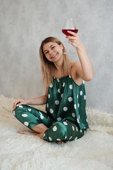 Girl in green pajamas in bed with a glass of red wine. Morning wine in bed. Vertical photo