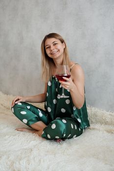 Girl in green pajamas in bed with a glass of red wine. Morning wine in bed. Vertical photo