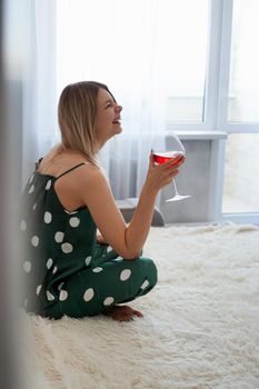 Girl in green pajamas in bed with a glass of red wine. Morning wine in bed. Vertical photo