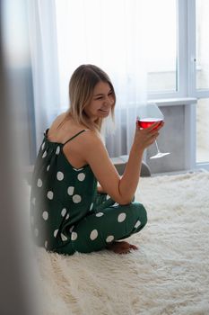 Girl in green pajamas in bed with a glass of red wine. Morning wine in bed. Vertical photo