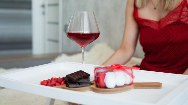 Breakfast for girlfriend. Valentines Day Morning. Wine and sweets on a white tray. Breakfast in bed. Girl in a red peignoir on the background