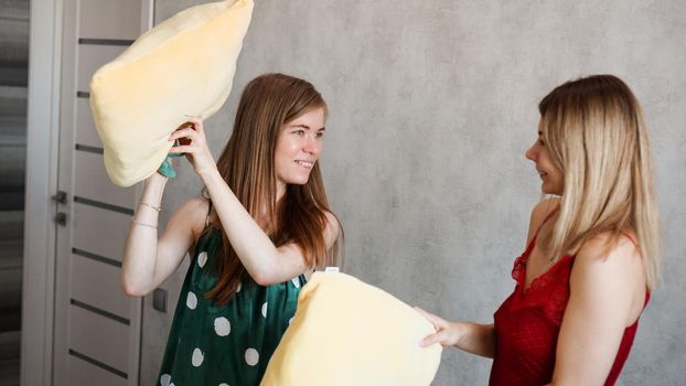 Two girl friends pillow fight in room at a pajama party