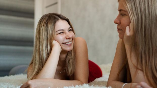 Happy friends lying in bed and talking and laughing