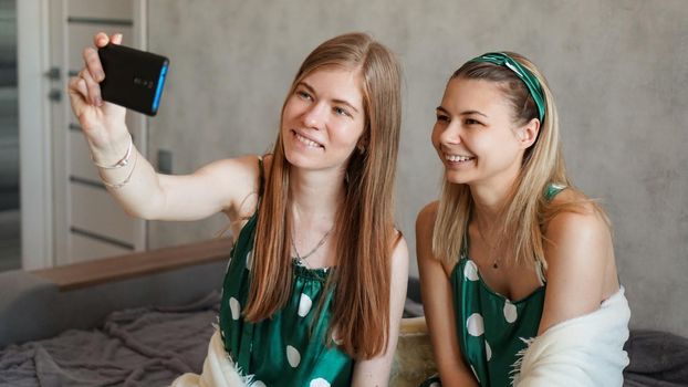 Two beautiful happy girlfriends taking selfie with smartphone at pajama party