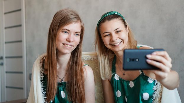 Two beautiful happy girlfriends taking selfie with smartphone at pajama party