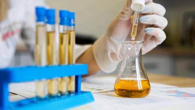 Woman making urine test with ph material in laboratory. Female hands in gloves with pipette and a flask of urine in the medical office