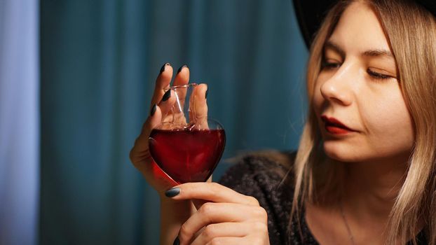 Cropped image of woman holding heart shaped glass jar of love potion. Beautiful young woman in a witch hat