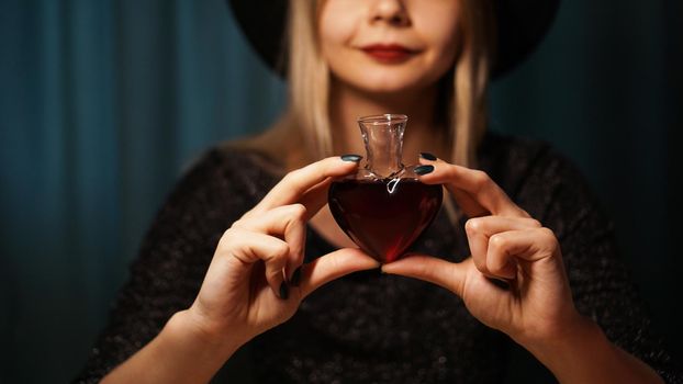 Cropped image of woman holding heart shaped glass jar of love potion. Beautiful young woman in a witch hat