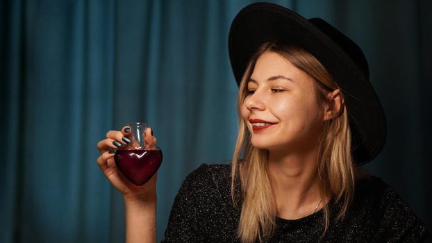 Cropped image of woman holding heart shaped glass jar of love potion. Beautiful young woman in a witch hat. Smiling blonde looking at the bottle