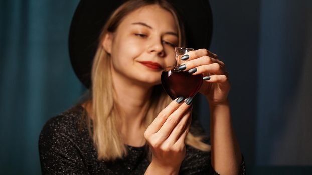 Cropped image of woman holding heart shaped glass jar of love potion. Beautiful young woman in a witch hat. Focus on Potion or Poison Vial