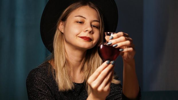 Cropped image of woman holding heart shaped glass jar of love potion. Beautiful young woman in a witch hat. Smiling blonde looking at the bottle