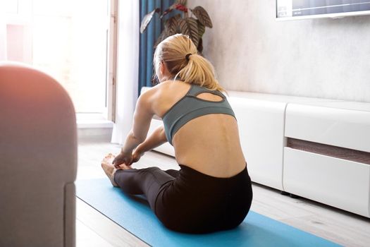 Fitness woman stretching legs sitting on the floor at home