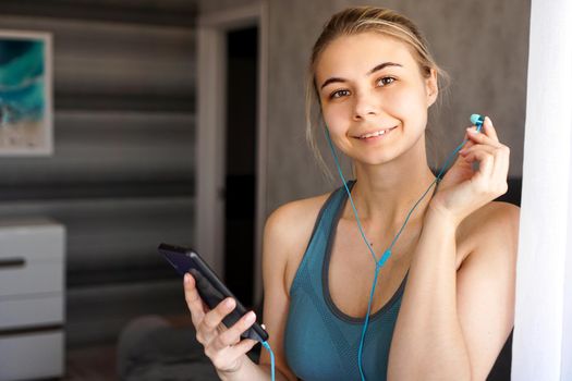 Young pretty sporty girl at home listens to music on headphones from smartphone