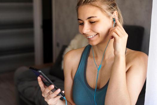 Young pretty sporty girl at home listens to music on headphones from smartphone