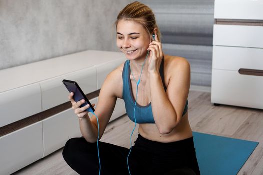 Take sport and add music. Female athlete with earphones enjoying the music playing and touching a screen of her phone while sitting on the floor.