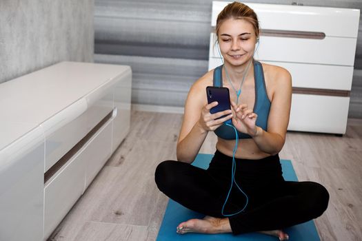 Take sport and add music. Female athlete with earphones enjoying the music playing and touching a screen of her phone while sitting on the floor.