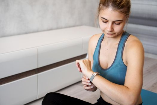 Portrait of young woman checking digital fitness tracker during self-training at home