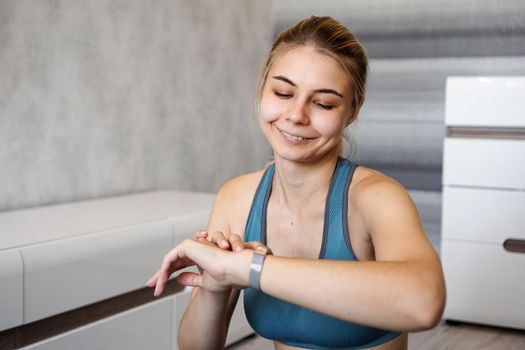 Portrait of young woman checking digital fitness tracker during self-training at home and smiling