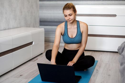 Girl training at home and watching videos on laptop before starting, training in living room