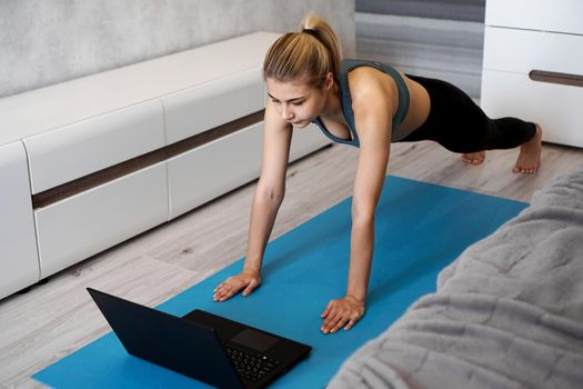 Fitness girl exercising watching on line videos on laptop in the living room at home