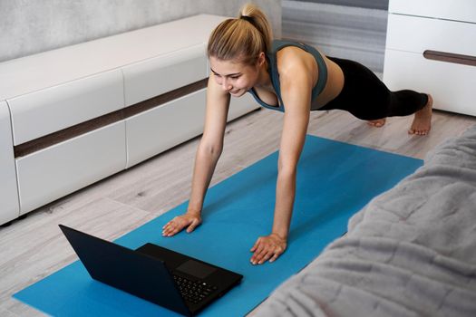 Fitness girl exercising watching on line videos on laptop in the living room at home