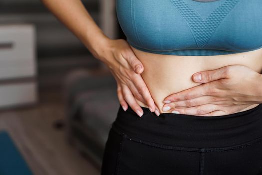 Close up of the woman holding her belly. Pain after home workout. Weight loss, slim body, healthy concept