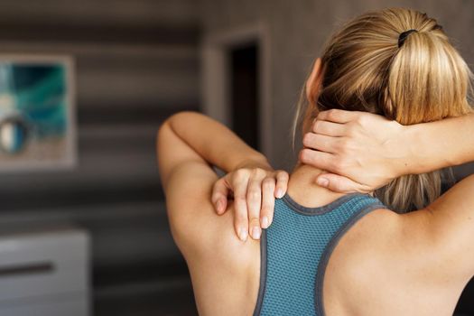 Sports injury concept. Athletic girl feeling pain in her neck against blurred background. Pain after home workout