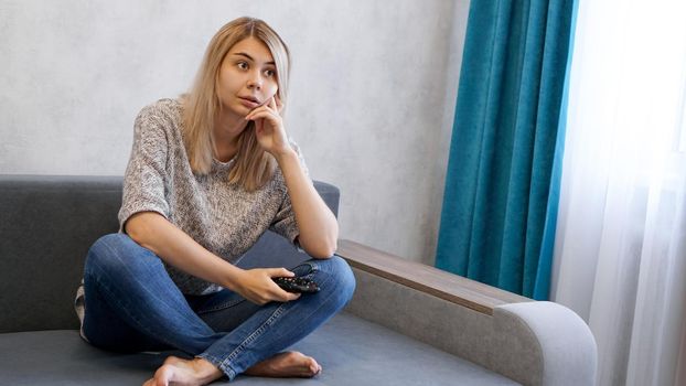 Young woman changing TV channels with remote control sitting on sofa at home