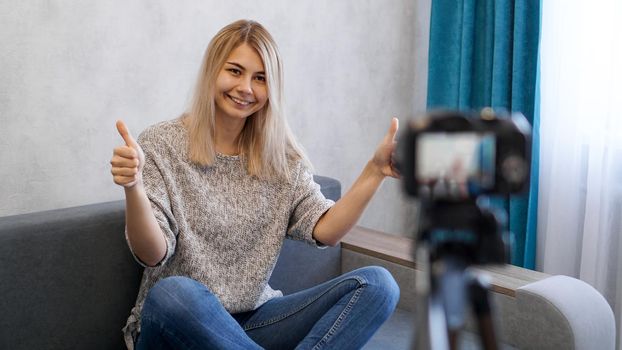 Wwoman or blogger with camera recording video and showing thumbs up at home