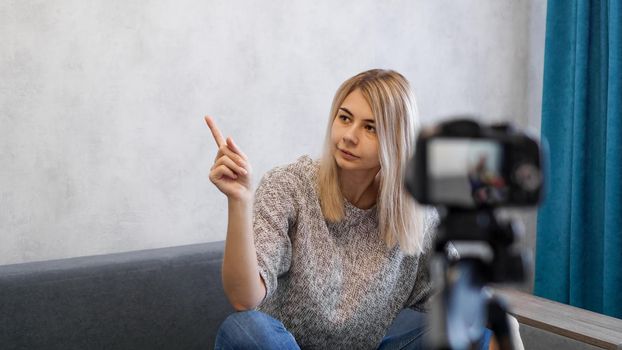 Young female blogger talks about business or records a lecture. Woman shows with on a gray wall. Place for information