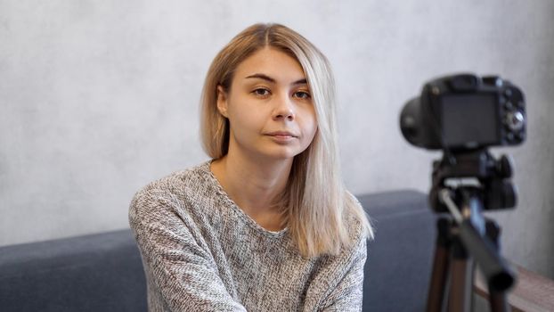 The woman blogger recorded a new video and turned off the camera on a tripod. She is tired and looks at the camera