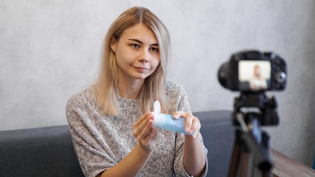 Cheerful female beauty blogger recording video at home. She shows lotion for skin.