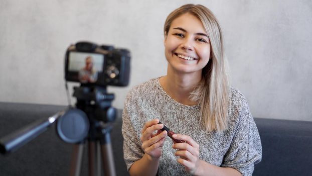 Vlogger female showing lipstick. Beauty blogger woman filming daily make-up routine tutorial near camera on tripod