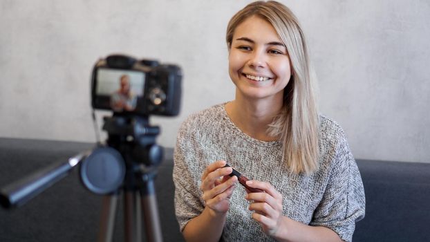 Vlogger female showing lipstick. Beauty blogger woman filming daily make-up routine tutorial near camera on tripod