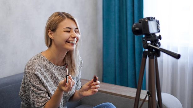 A beauty blogger or video blogger tells and shows subscribers how to do makeup. Young woman paints lips and laughs at a joke