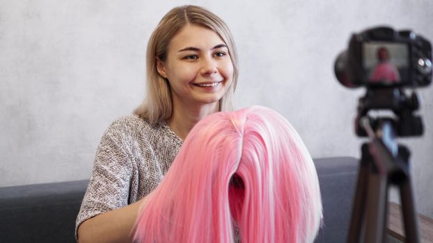 Woman blogger records video. She talks about haircuts and shows a pink wig. Stylist and fashion consultant recording the lecture