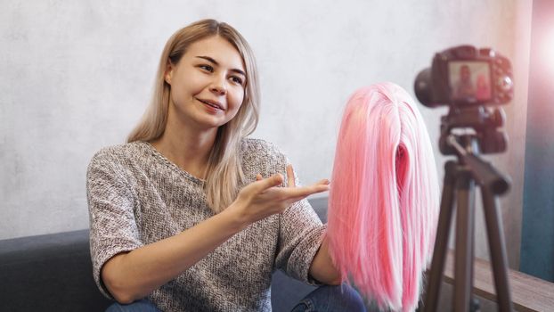 Woman blogger records video. She talks about haircuts and shows a pink wig. Stylist and fashion consultant recording the lecture