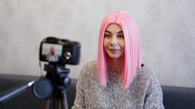 Happy blogger in pink wig in front of the camera on a tripod. She records a video