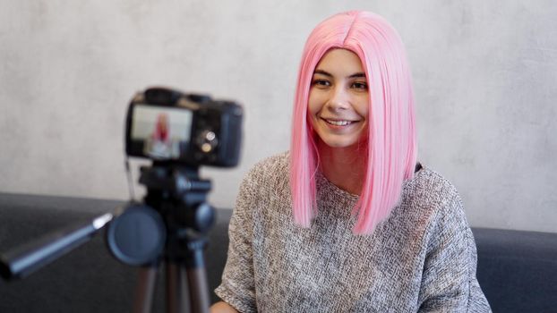 Happy blogger in pink wig in front of the camera on a tripod. She records a video