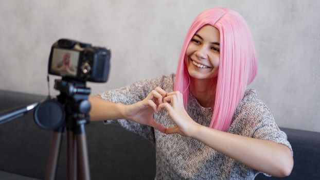 Woman looks at camera and shows heart shape sign with her palms. Girl with pink hair, freelancer, blogger