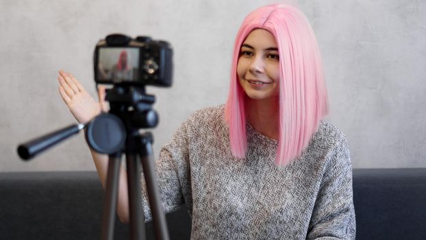 Happy girl blogger in pink wig in front of the camera on a tripod. She records a video blog and communicates with subscribers on social networks