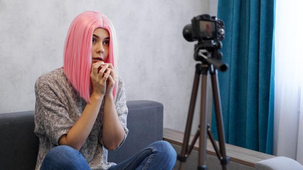 Young female blogger in pink wig with camera vlogging stressed