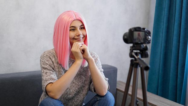 Happy girl blogger in pink wig in front of the camera on a tripod. She records a video blog