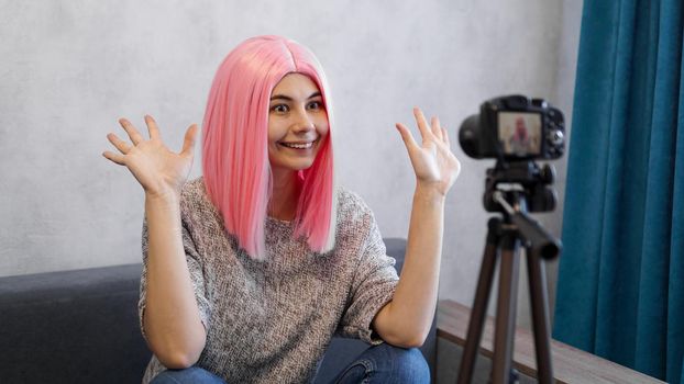 Happy girl blogger in pink wig in front of the camera on a tripod. She records a video blog